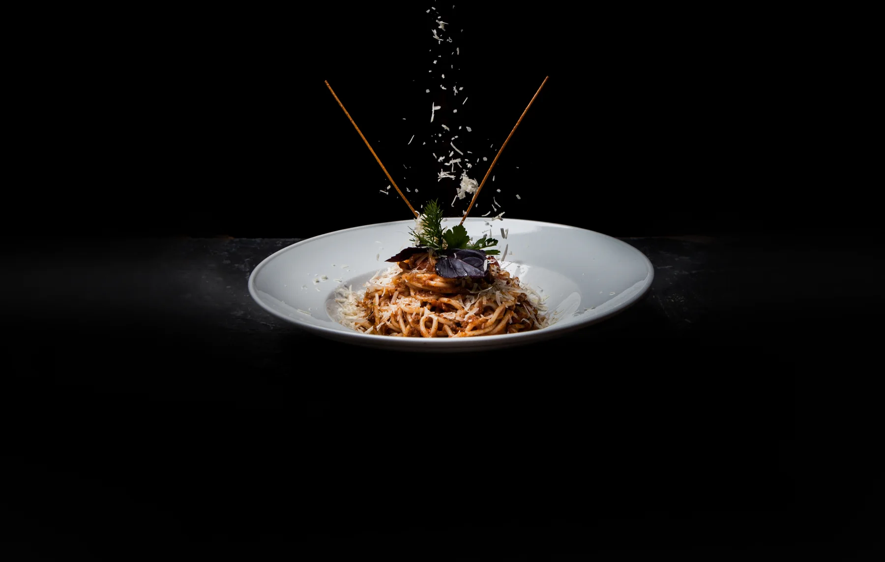 A plate of spaghetti in a dark studio, with grated cheese falling over it